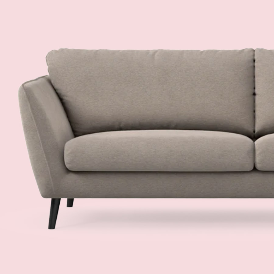 En beige 3-sitssoffa med vinkade armstöd mot en ljusrosa bakgrund.