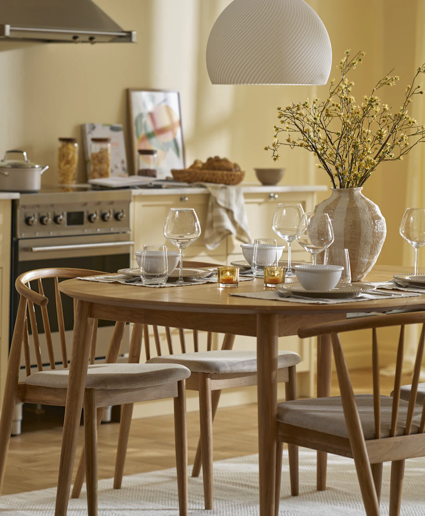 Ett matbord i ek med fyra stolar står i ett gult kök.