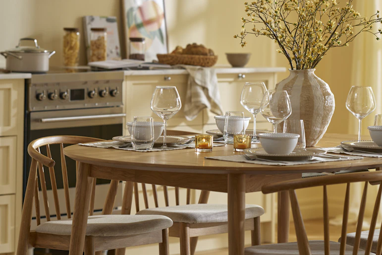 Ett matbord i ek med fyra stolar står i ett gult kök.