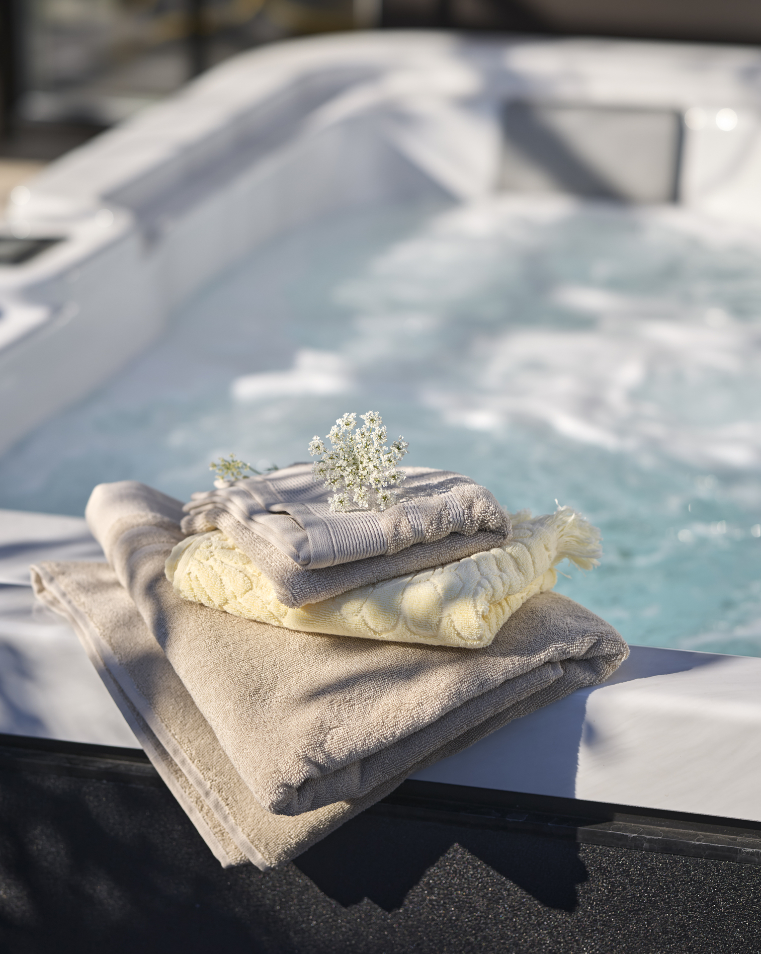 En hög med ihopvikta handdukar i beiget och gult ligger på en kant till en bubbelpool