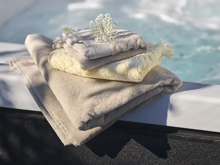 En hög med ihopvikta handdukar i beiget och gult ligger på en kant till en bubbelpool