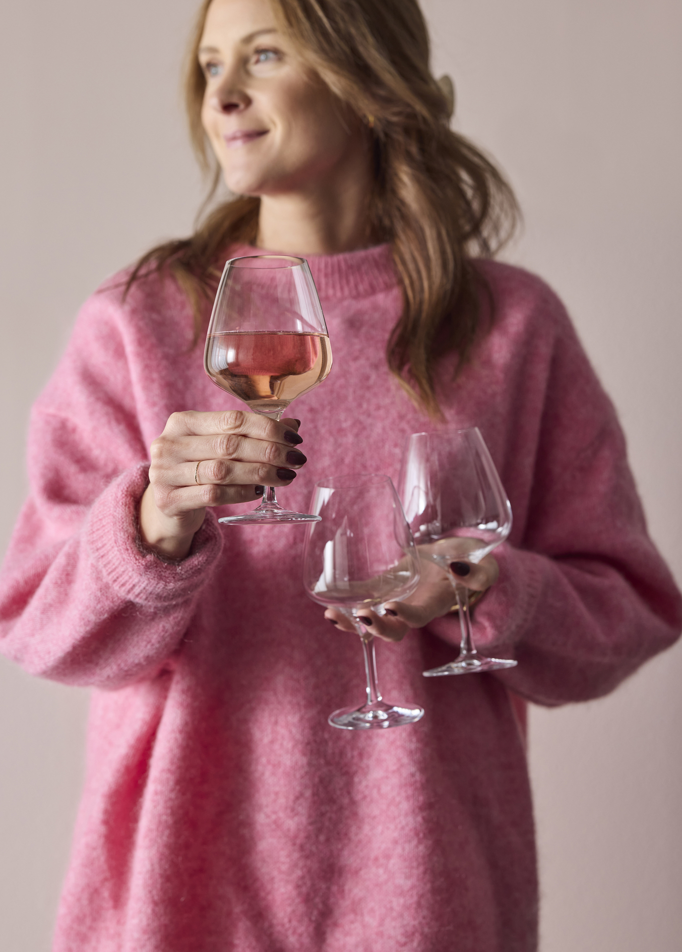 En kvinna i rosa tröja håller i tre vinglas.