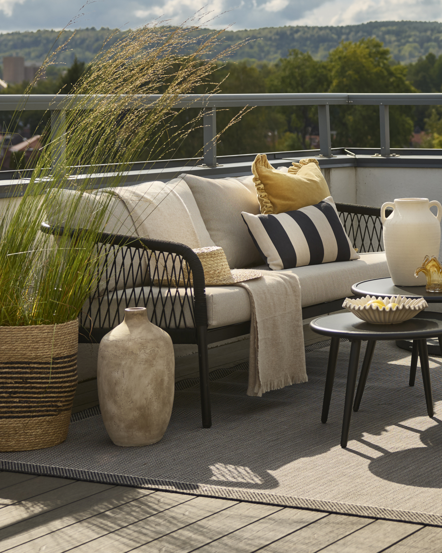 3-sits utesoffa med svart repflätning och beiga kuddar står på en balkong.