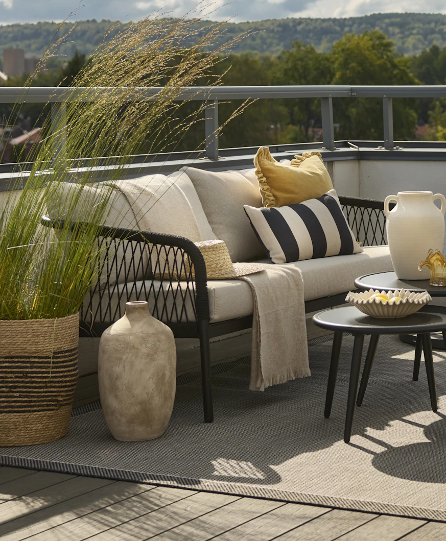 3-sits utesoffa med svart repflätning och beiga kuddar står på en balkong.