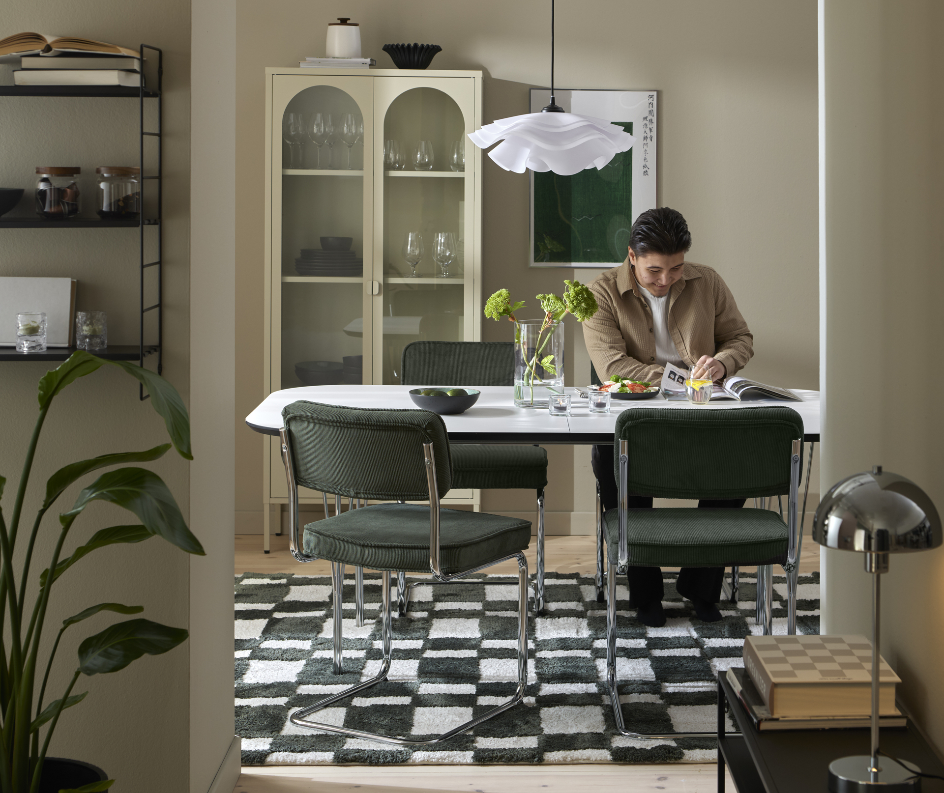 En man sitter vid ett vitt matbord med fyra stolar i grönt manchestertyg. Bordet står på en grön- och vitrandig matta.