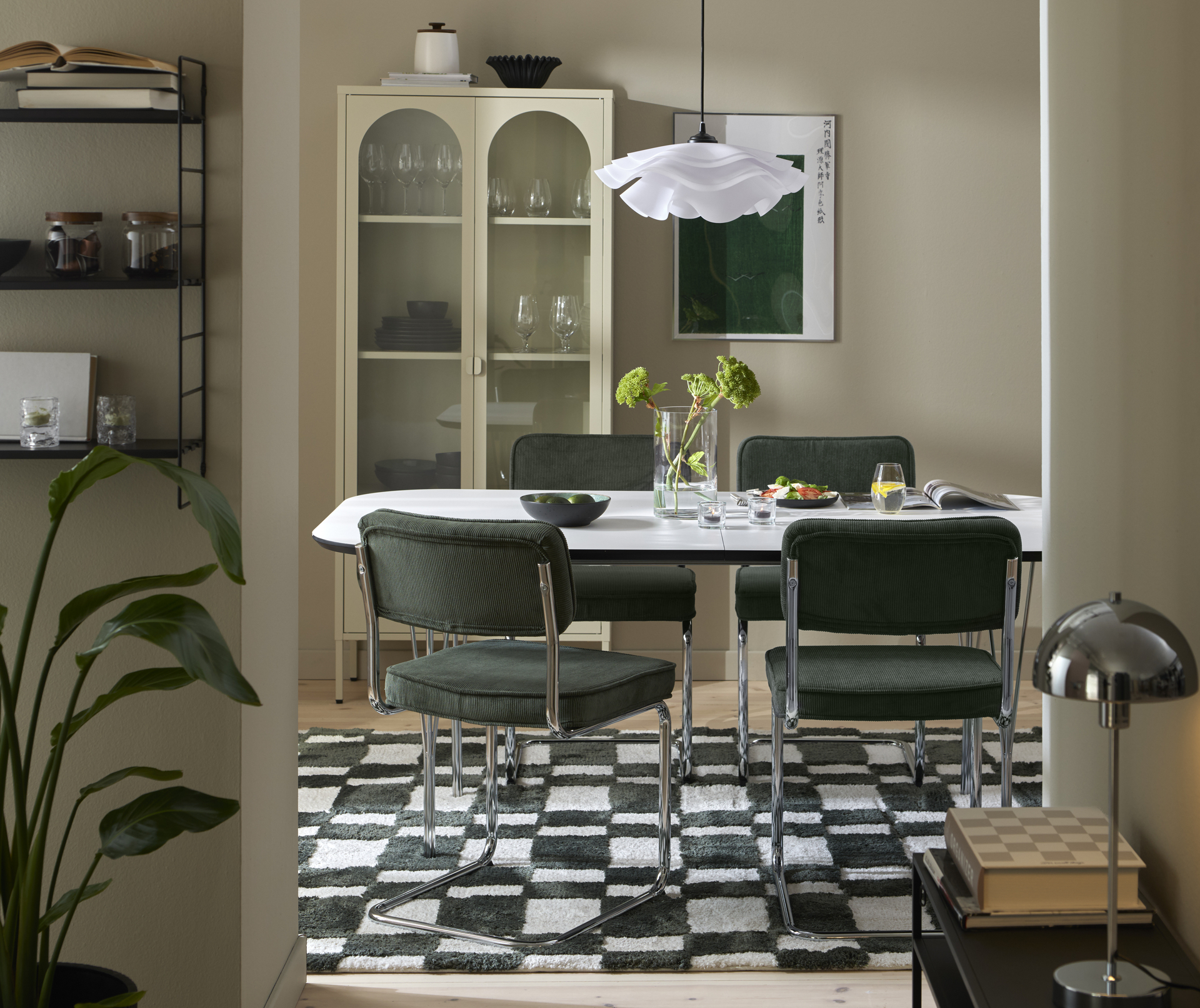 I ett ljust matrum står ett vitt matbord med fyra stolar i grönt manchestertyg. Bordet står på en grön- och vitrandig matta.