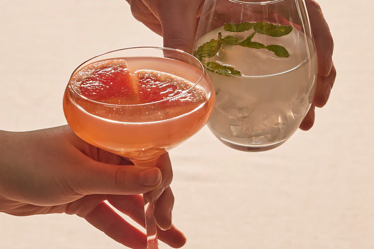 Flera händer stäcker sig över ett bord och skålar i glas fyllda med olika sorters drinkar