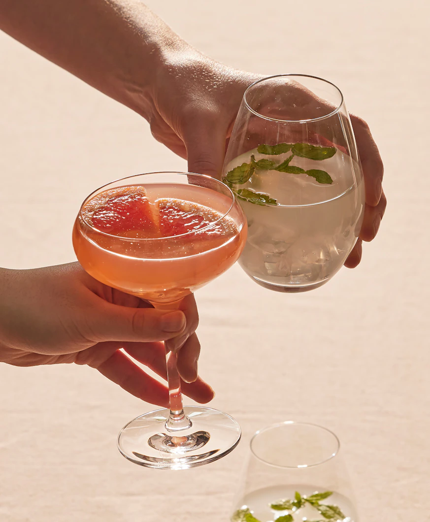 Flera händer stäcker sig över ett bord och skålar i glas fyllda med olika sorters drinkar