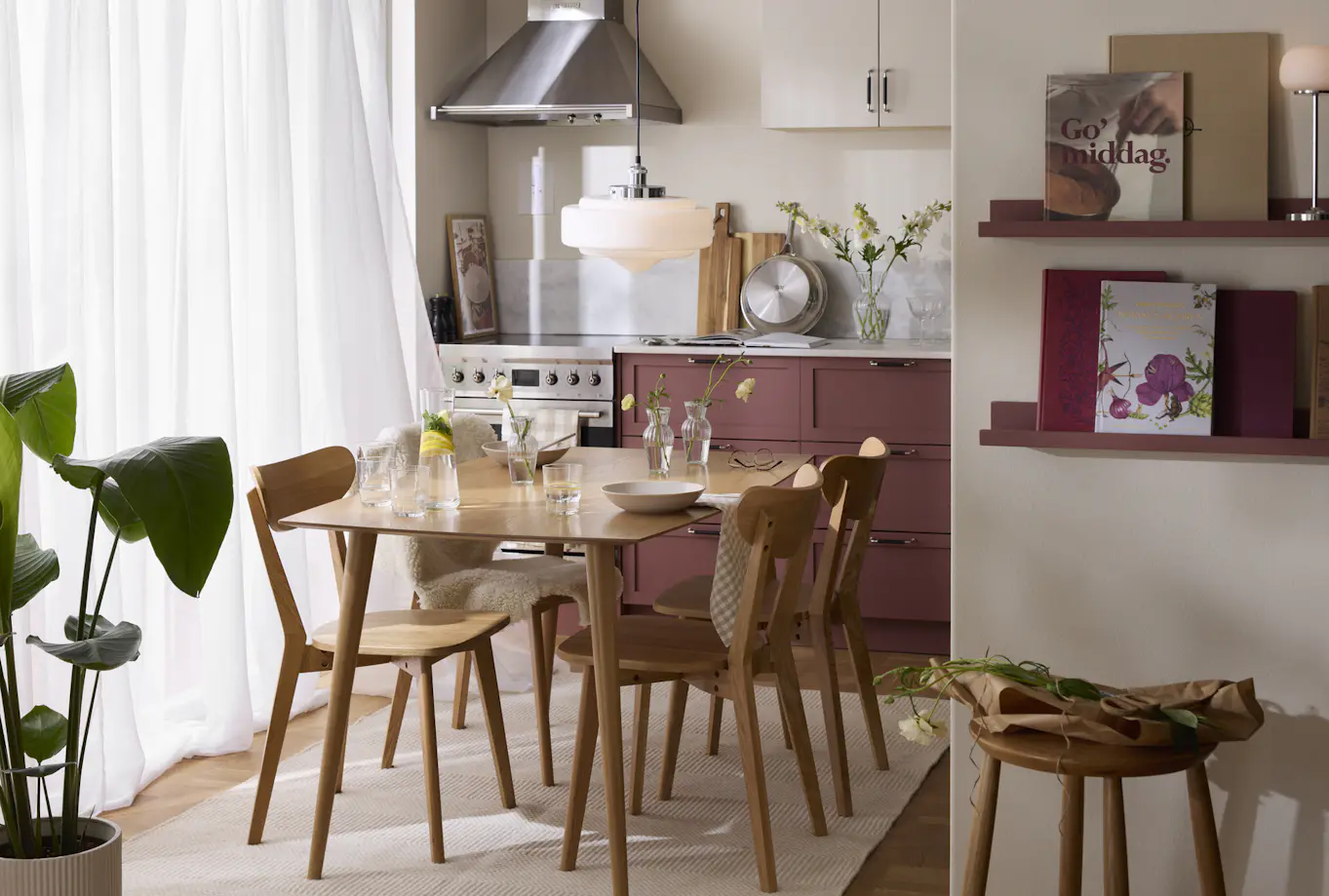 I ett ljust kök med mörkrosa köksluckor står ett matbord i ek med fyra stolar.