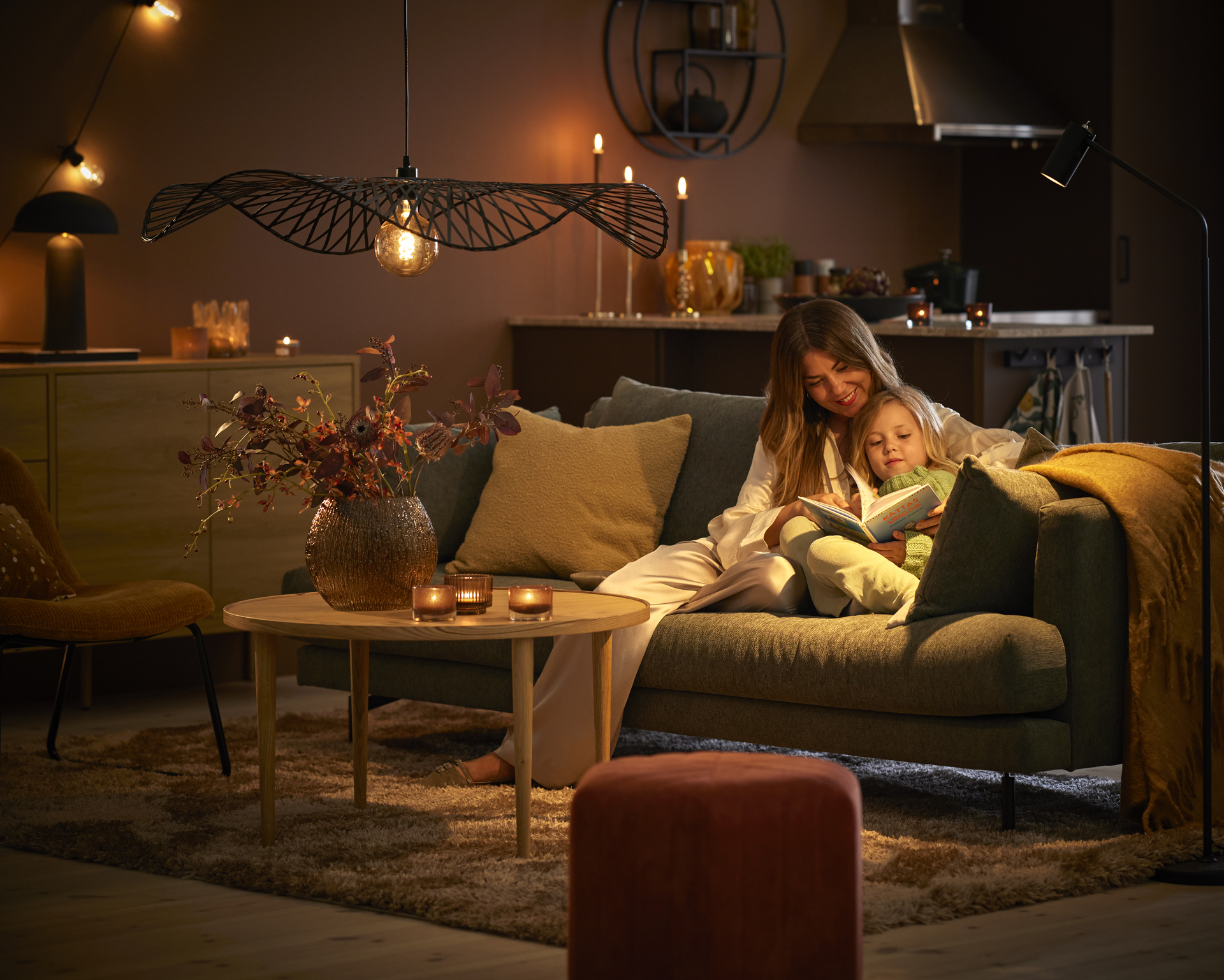 I en soffa i ett mysigt belyst vardagsrum sitter en kvinna och läser med ett barn i famnen.