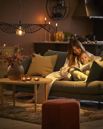 I en soffa i ett mysigt belyst vardagsrum sitter en kvinna och läser med ett barn i famnen.