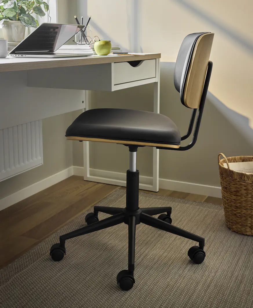 Svart höj- och sänkbar kontorsstol står vid ett vitt skrivbord.