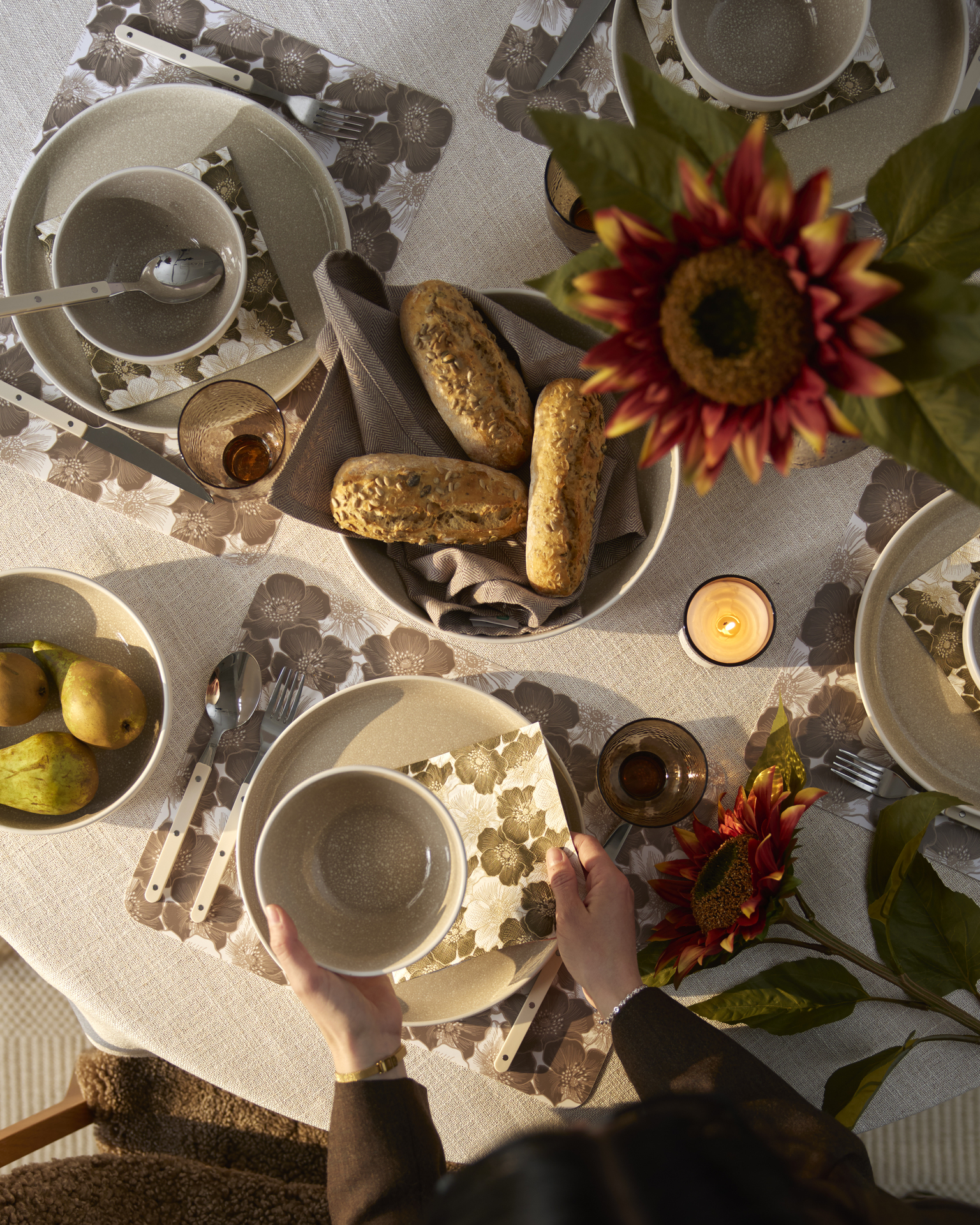 Uppduktat frukostbord med beige servis, beige duk på bord och solros i vas. Färska frallor och päron på fat