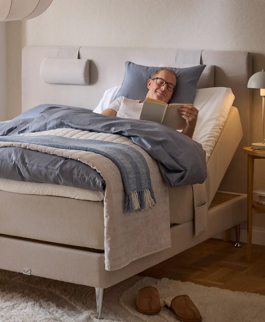 En man ligger och läser i en beige ställbar säng