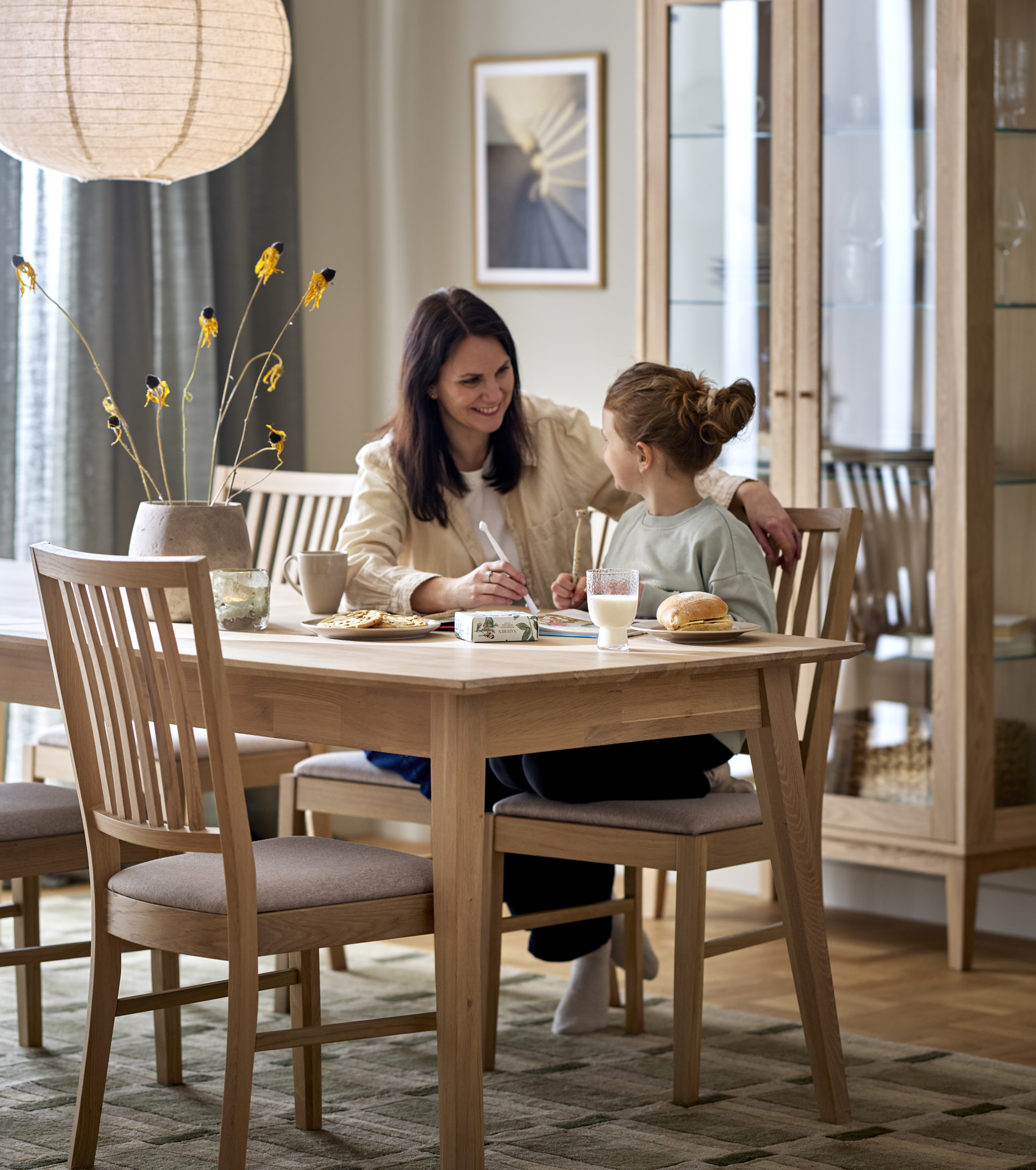 En mamma och dotter sitter vid en matgrupp i ljust trä