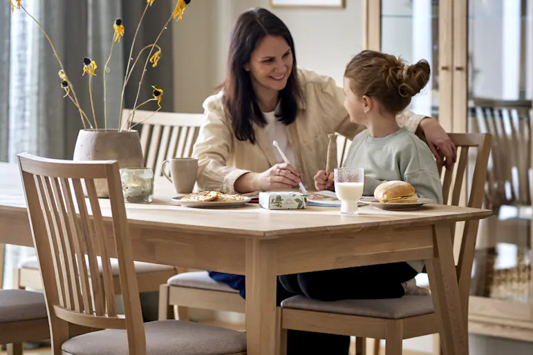 En mamma och dotter sitter vid en matgrupp i ljust trä