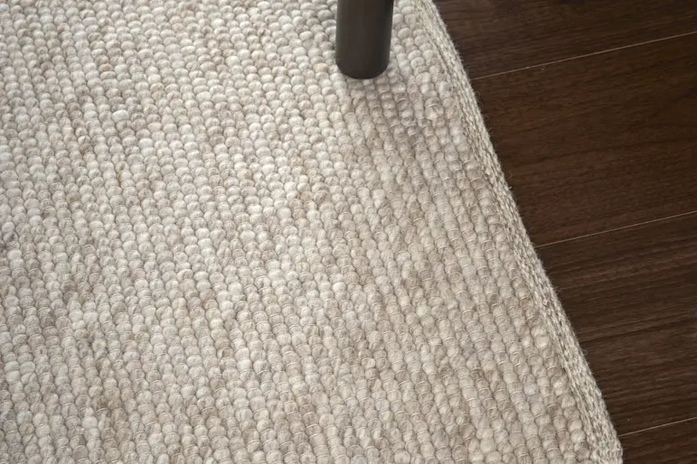En beige ullmatta ligger på ett mörkt trägolv