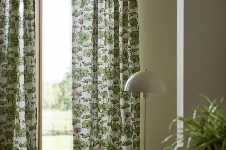 I ett fönster hänger en gardin med grönt, naturnära mönster