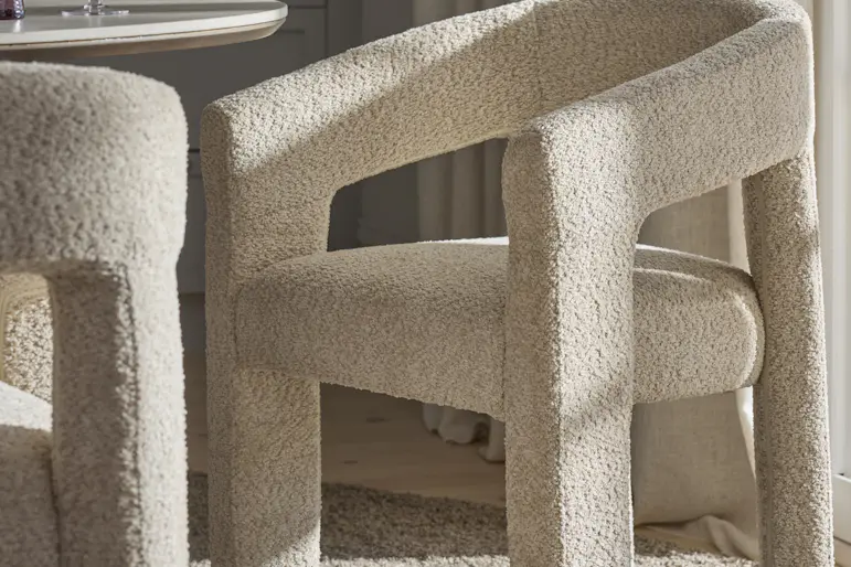 Trendig karmstol i beige bouclé står vid ett runt bord.