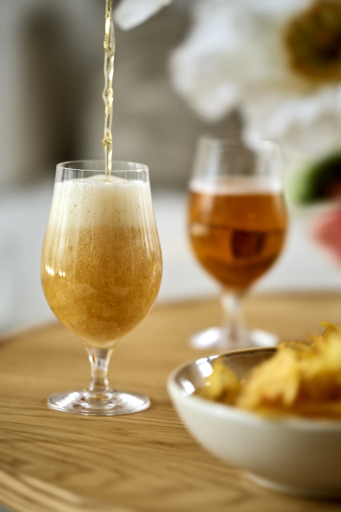Två ölglas på ett bord, det främre glaset håller just på att fyllas på i en stråle uppifrån.
