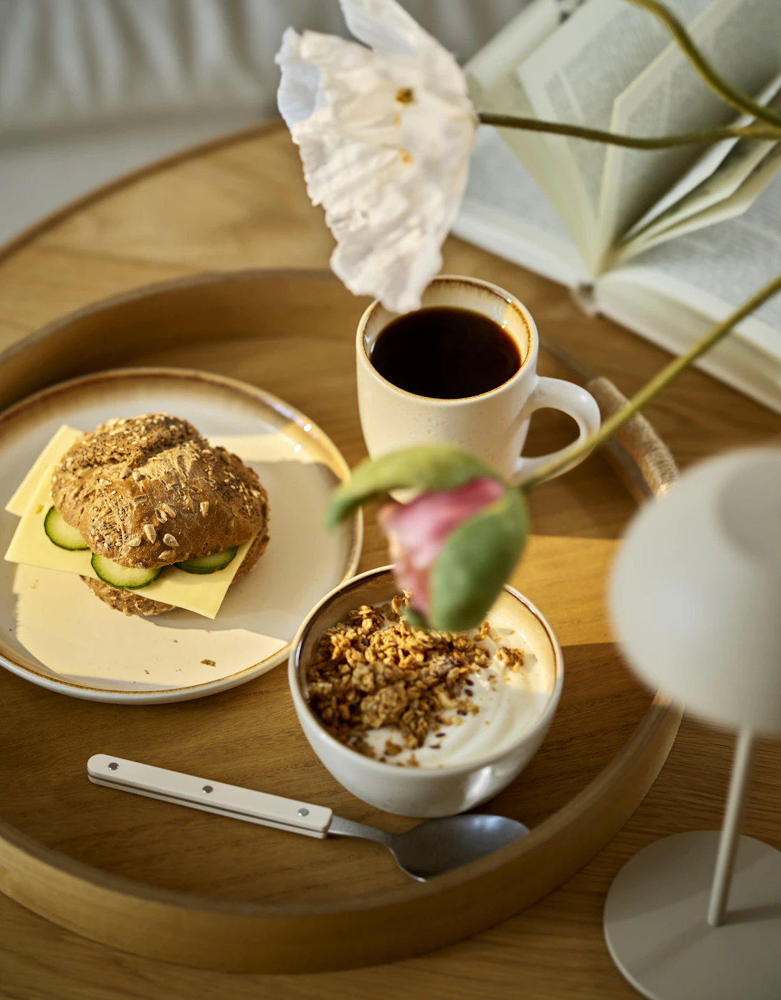 Bricka med fat av porslin med smörgåsar på, i en djup skål finns granola och yoghurt och en kopp kaffe intill.