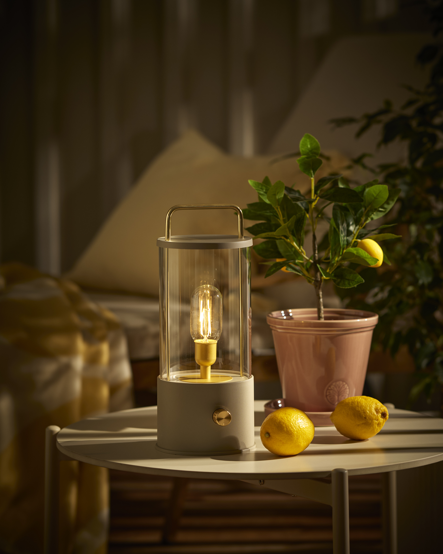 En portabel beige bordslampa står på ett utesoffbord intill en kruka med en citrusväxt.
