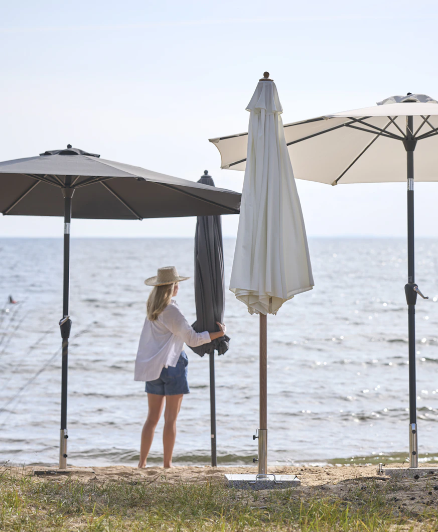 en kvinna i vit skjorta och shorts står på stranden bland flera parasoll i olika färger