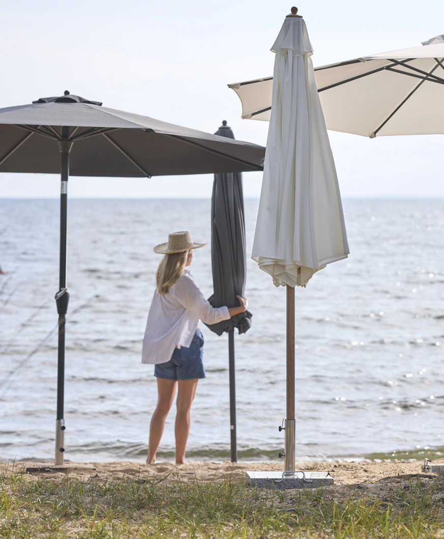 en kvinna i vit skjorta och shorts står på stranden bland flera parasoll i olika färger