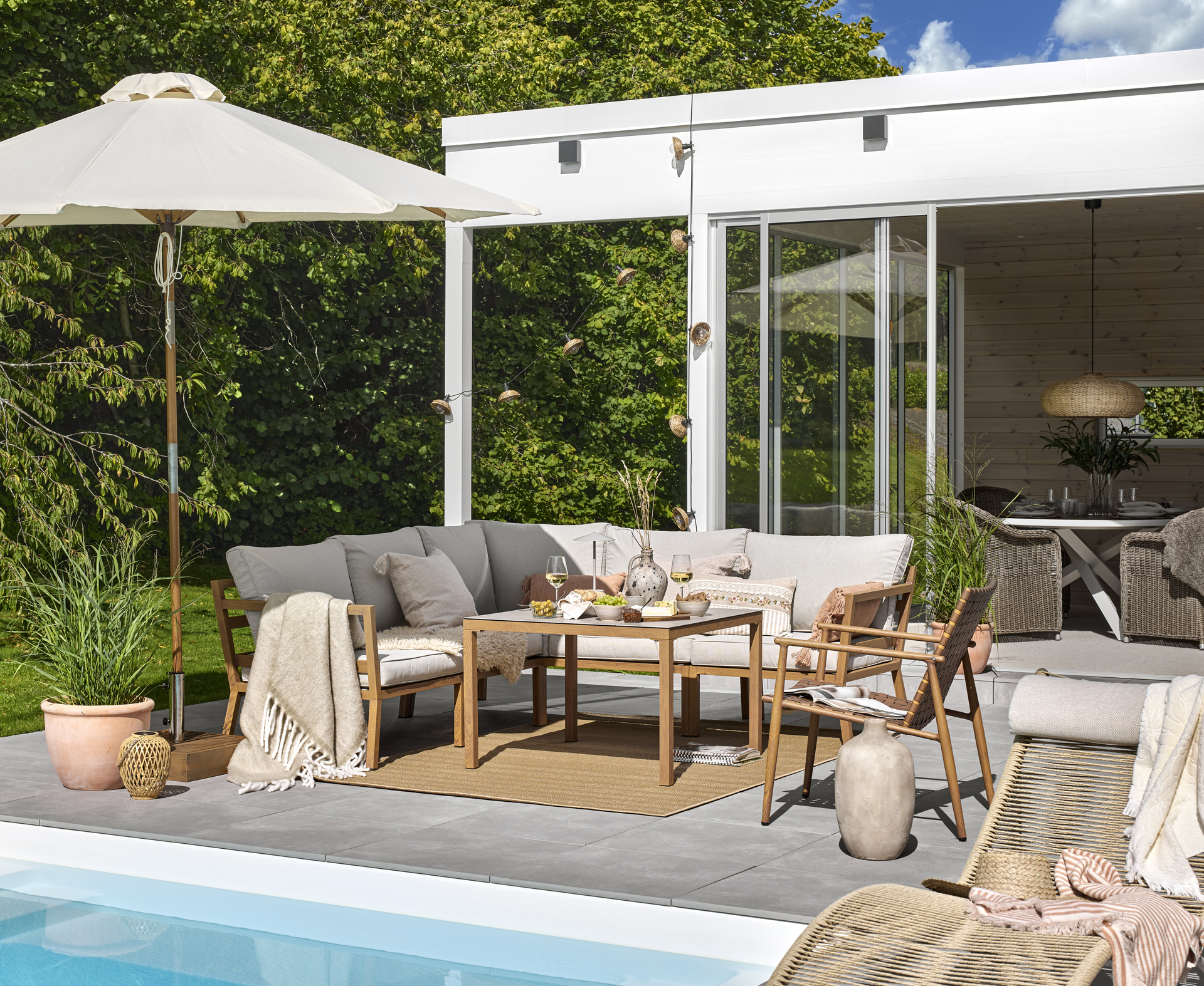 En loungegrupp står utomhus vid en pool tillsammans med ett parasoll 