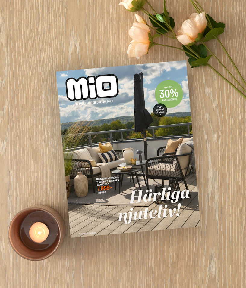 På ett ljust träbord ligger Mios utelivsbilaga intill ett ljus och en blomma.