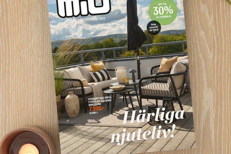 På ett ljust träbord ligger Mios utelivsbilaga intill ett ljus och en blomma.