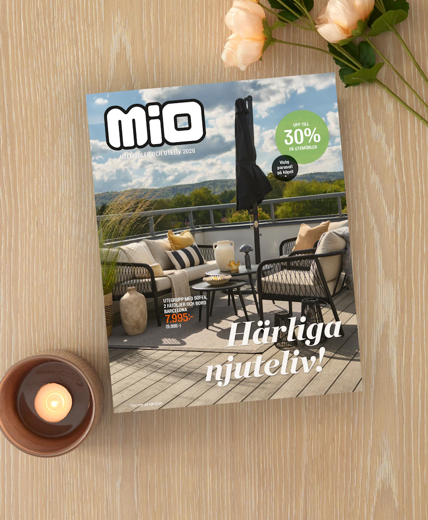På ett ljust träbord ligger Mios utelivsbilaga intill ett ljus och en blomma.