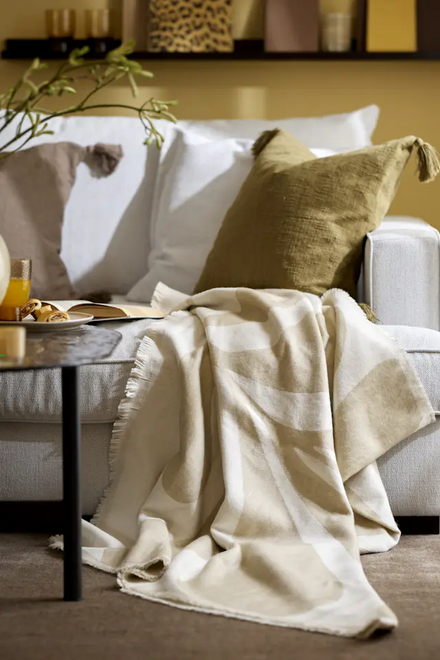Beige filt på vit soffa, olivfärgad kudde