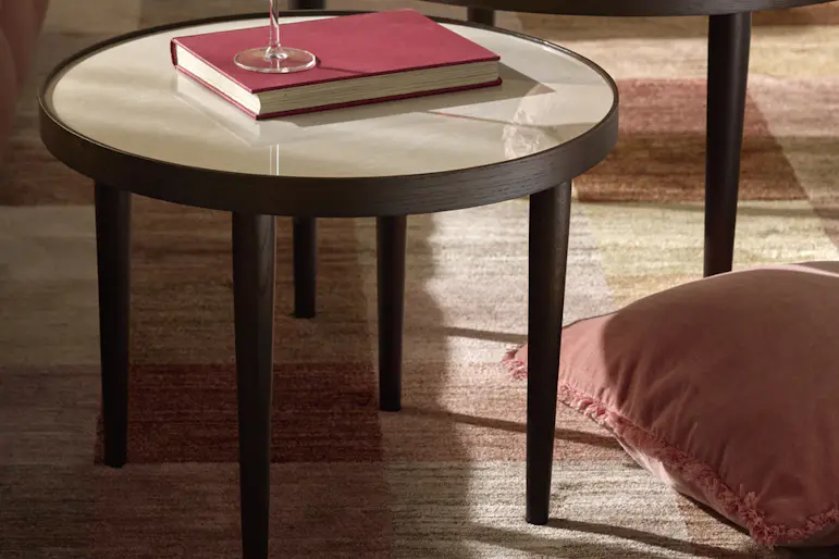 Grupp med två soffbord av rökfärgade ekfaner med bordsskivor av beige keramik står på en rutig matta. Bredvid dem står en röd soffa.