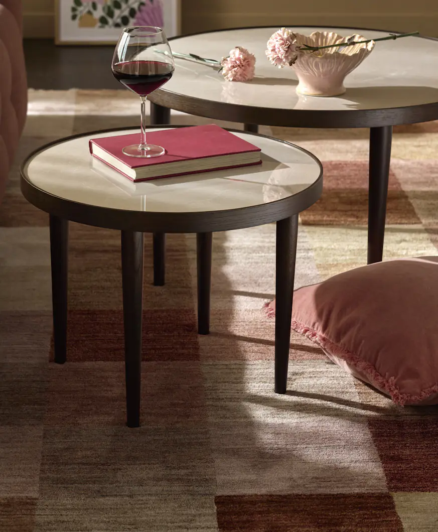 Grupp med två soffbord av rökfärgade ekfaner med bordsskivor av beige keramik står på en rutig matta. Bredvid dem står en röd soffa.