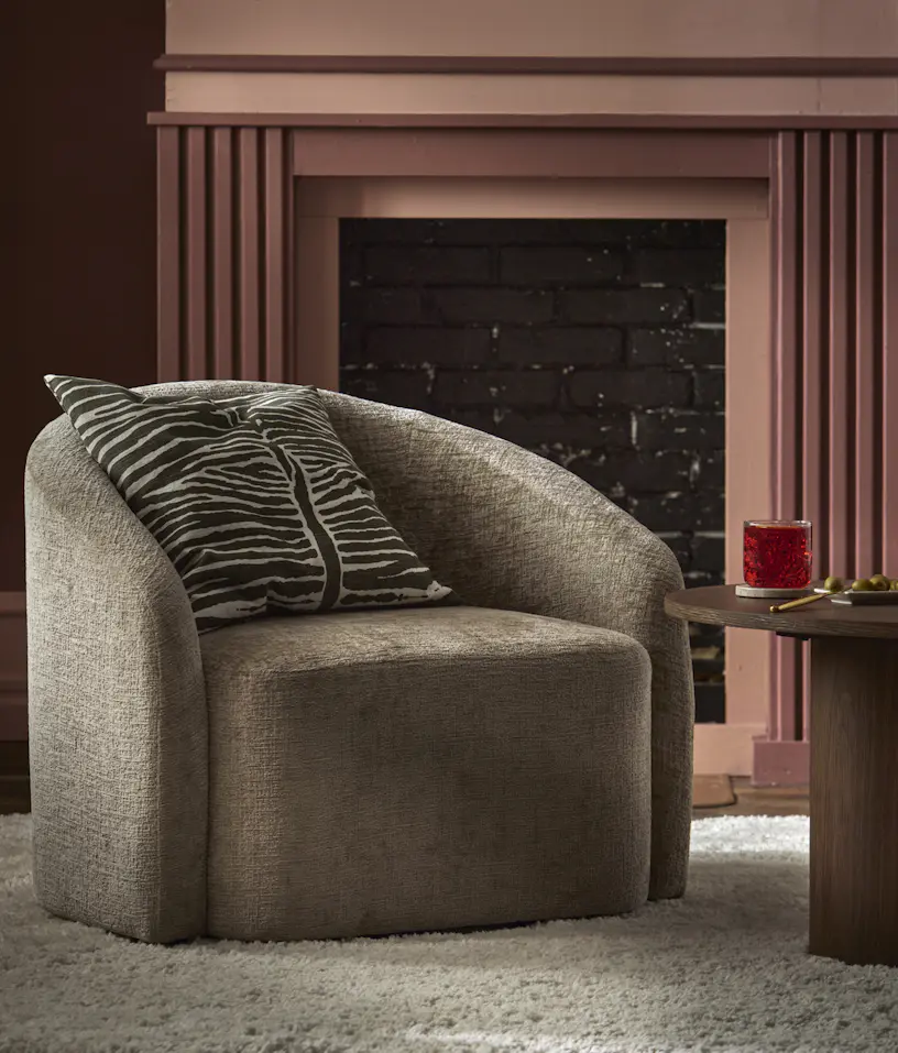 Beige fåtölj med zebramönstrad kudde i grönt och vitt står framför en rosa eldstad.