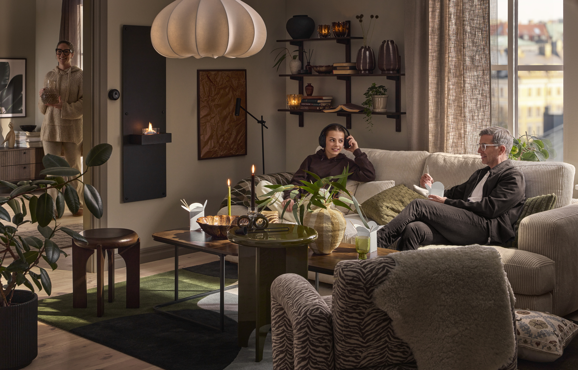 I en beige soffa sitter en man och äter och en tjej och lyssnar på musik i hörlurar.