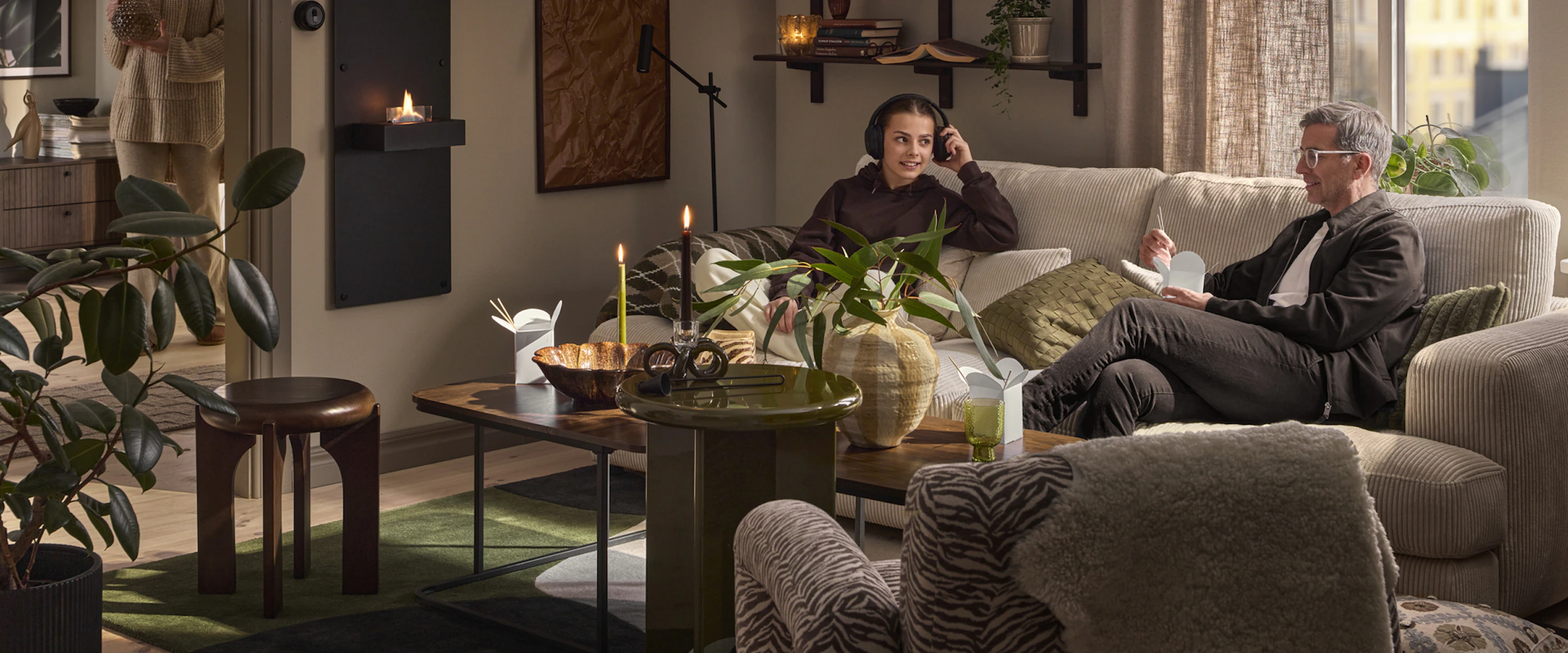 I en beige soffa sitter en man och äter och en tjej och lyssnar på musik i hörlurar.