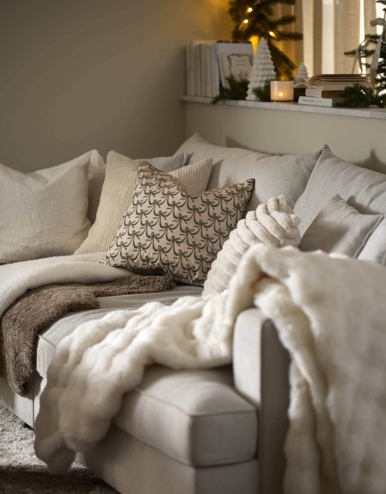 Olika ljusa kuddar och plädar ligger i en offwhite soffa.