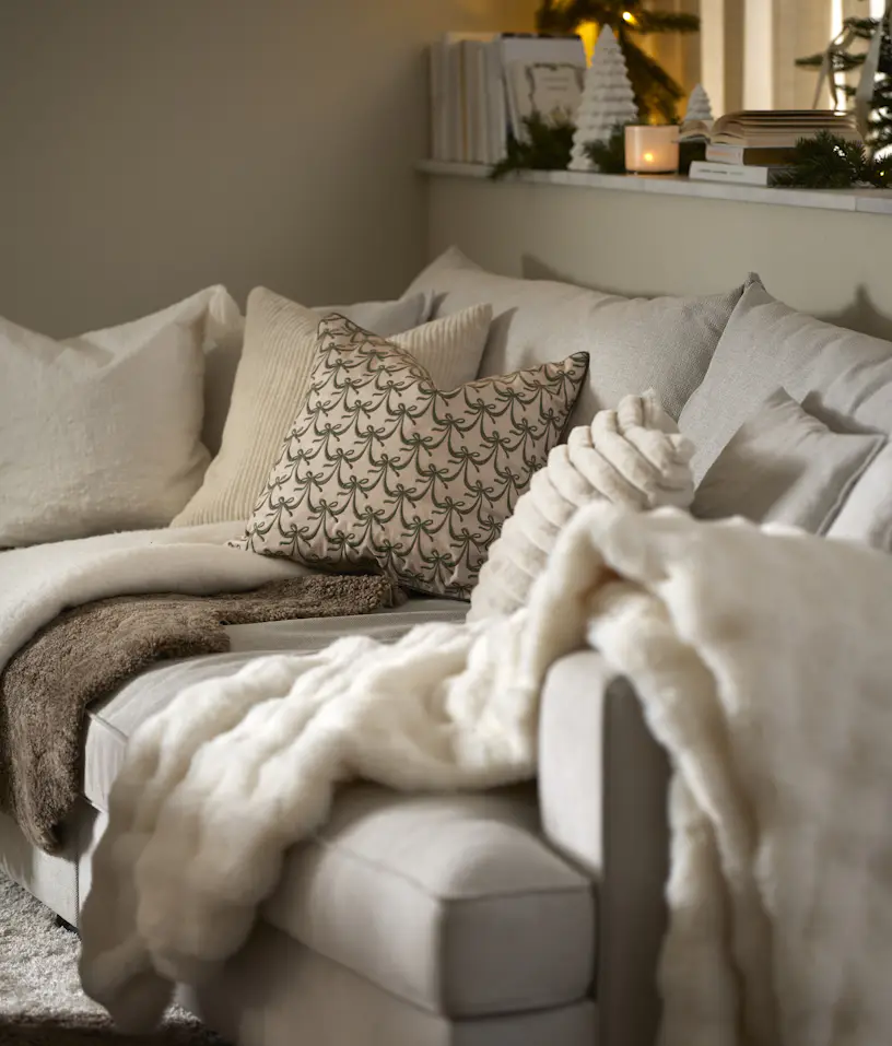 Olika ljusa kuddar och plädar ligger i en offwhite soffa.
