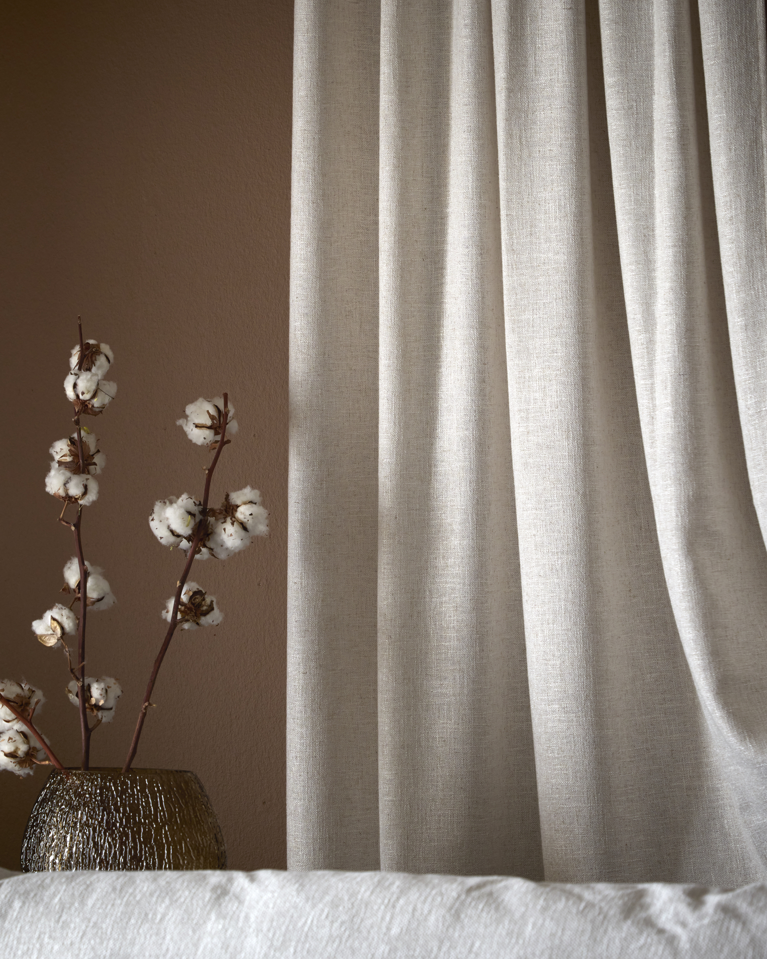 En beige gardin hänger framför en roströd vägg