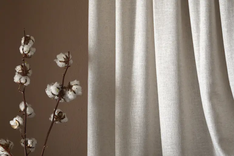 En beige gardin hänger framför en roströd vägg