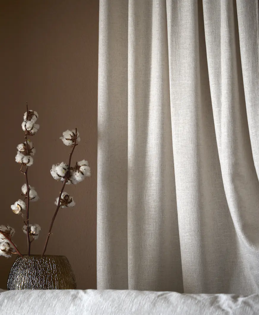 En beige gardin hänger framför en roströd vägg