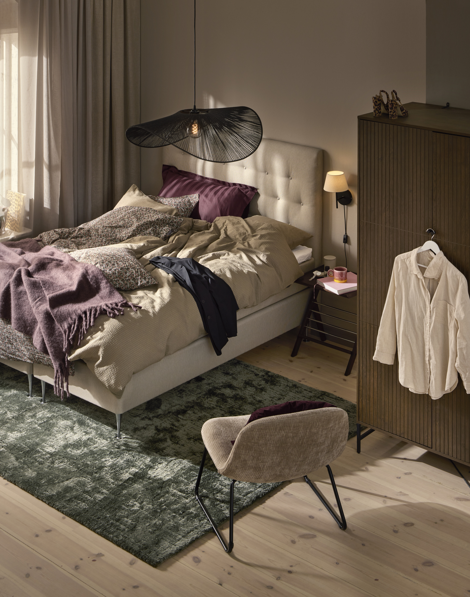 Beige 160-säng med pikerad gavel och sängkläder i matchande toner, en beige fåtölj och en garderob i mörkt trä står i ett litet sovrum.