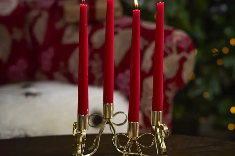 Fyra röda stearinljus står i en rund, guldig ljusstake som ser ut som rosetter. Framför står julgodis på en assiett.