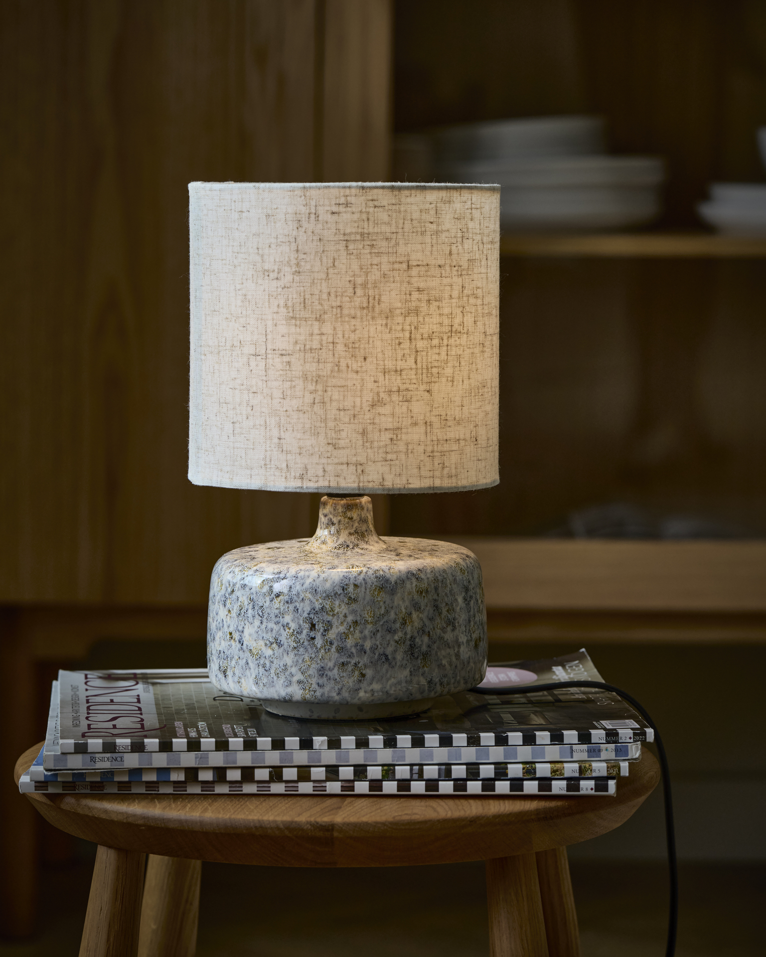 Bordslampa med beige textilskärm och keramikfot står på en pall.