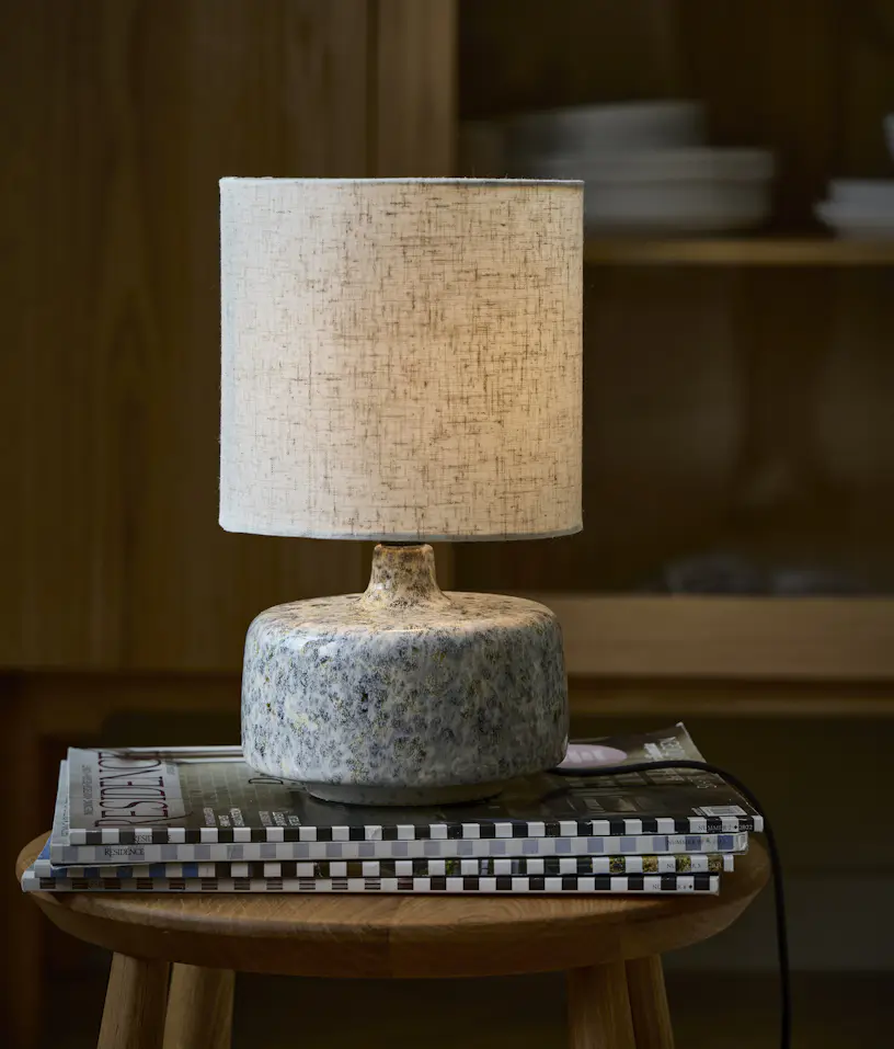 Bordslampa med beige textilskärm och keramikfot står på en pall.