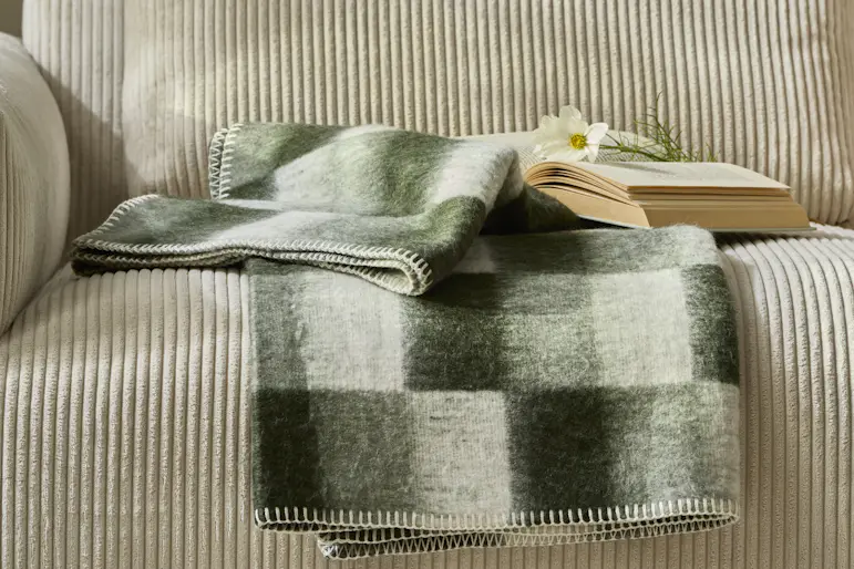 En grön-rutig pläd ligger på en beige soffa i manchester