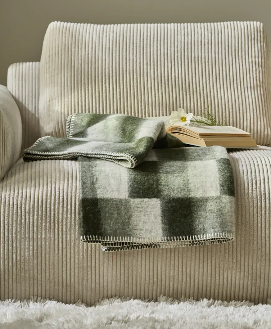 En grön-rutig pläd ligger på en beige soffa i manchester