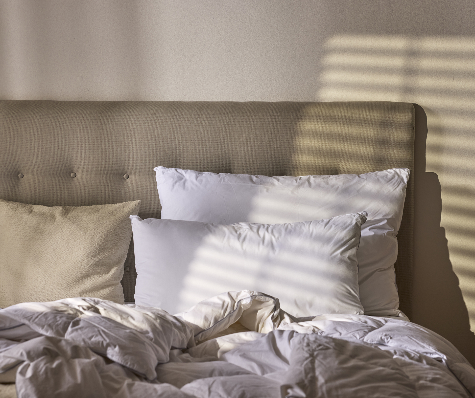 Två vita kuddar ligger i en säng mot en beige sänggavel